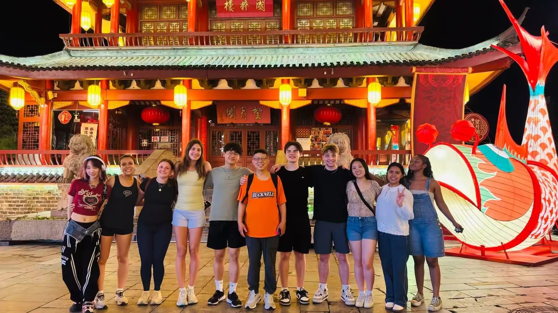 Students and Professor Lin in front of an illuminated traditional building during an evening cultural excursion